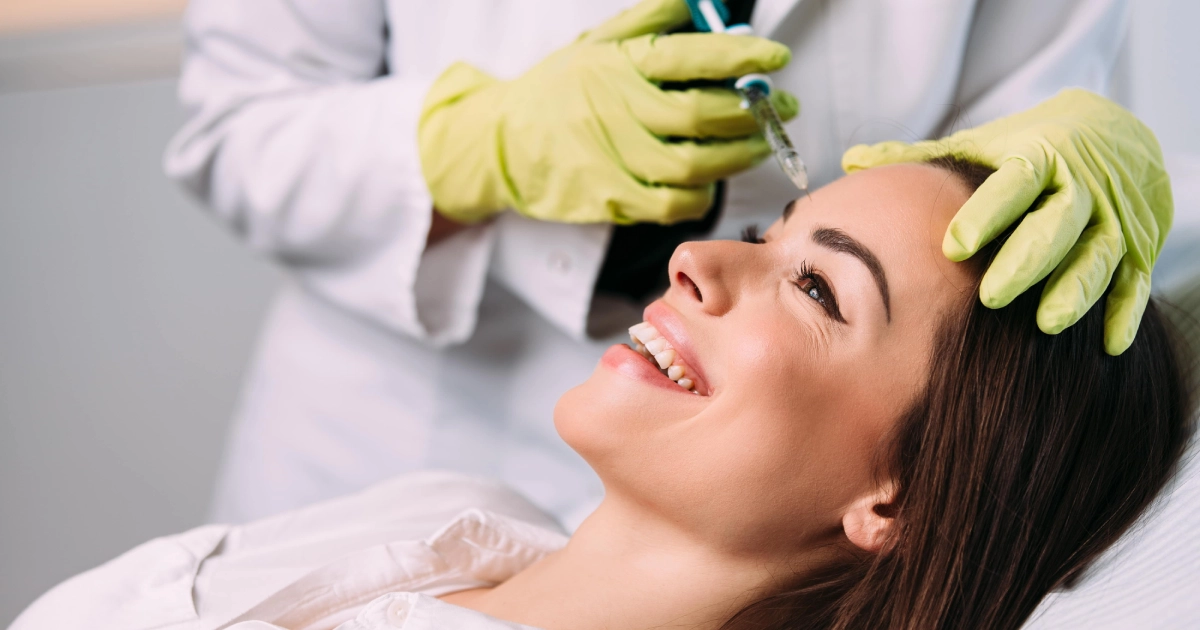 Smiling woman receiving a forehead injection from a medical professional wearing gloves during a Botox or Dysport treatment in Greenwich